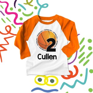 May include: White and orange long-sleeve baseball t-shirt with a basketball graphic and the number "2" in black. The text "Happy Birthday Boy" is repeated around the basketball. The name "Cullen" is printed below the basketball.