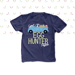 May include: Navy blue t-shirt featuring a light blue truck graphic filled with Easter eggs. The text "Expert Egg Hunter Payton" is printed below the truck. The background has a pattern of bunny ears.