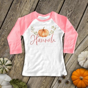 Pode incluir: Uma camisa de manga comprida branca e rosa com uma ab&oacute;bora e a palavra "Hairfall" em letras de glitter rosa.