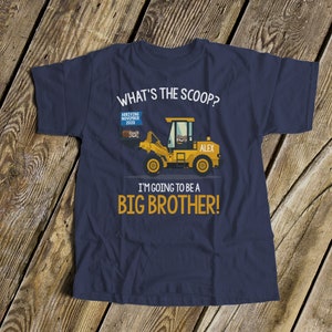 Puede incluir: Camiseta azul marino con un gr&aacute;fico de veh&iacute;culo de construcci&oacute;n amarillo. El texto incluye "WHAT'S THE SCOOP?" y "I'M GOING TO BE A BIG BROTHER!" con "ARRIVING NOVEMBER 2020" y el nombre "ALEX".