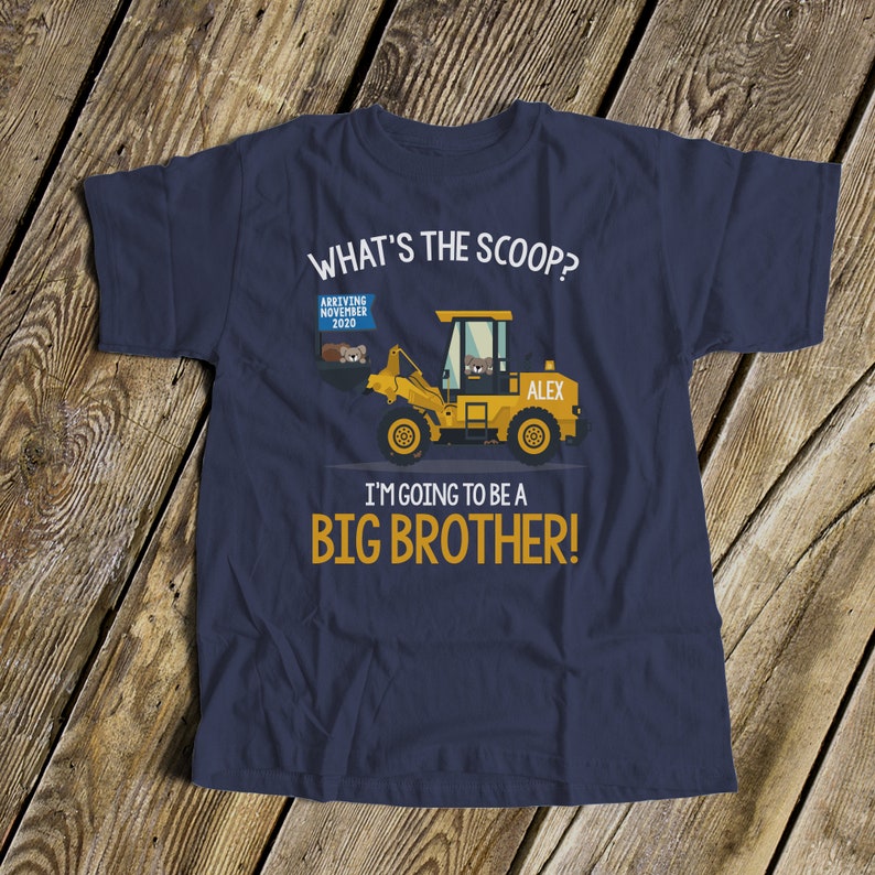 Puede incluir: Camiseta azul marino con un gr&aacute;fico de veh&iacute;culo de construcci&oacute;n amarillo. El texto incluye "WHAT'S THE SCOOP?" y "I'M GOING TO BE A BIG BROTHER!" con "ARRIVING NOVEMBER 2020" y el nombre "ALEX".
