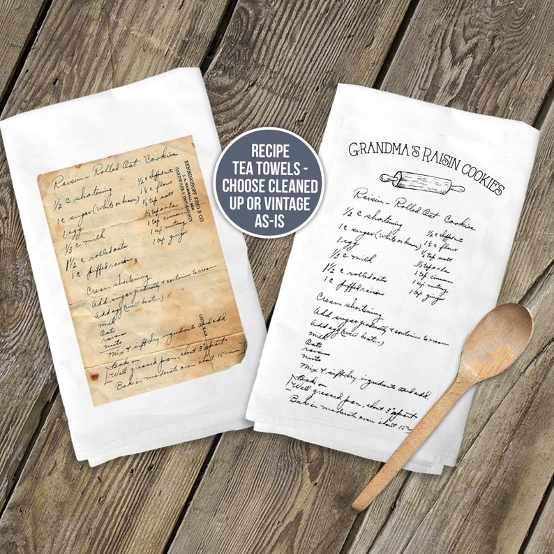 May include: Two white tea towels featuring a printed recipe for Raisin Rolled Oat Cookies. One towel displays a vintage, aged paper look, while the other shows a clean, black-ink version with a rolling pin graphic. A wooden spoon rests nearby.