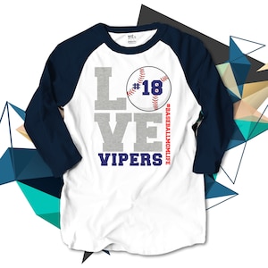 May include: White baseball t-shirt with a navy blue raglan sleeve. The shirt has a gray graphic that says "LOVE" with a baseball graphic that says "#18" and "VIPERS" below. The text "#BASEBALLMOMLIFE" is on the side of the baseball graphic.