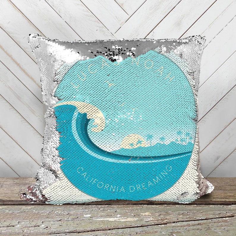 May include: A silver sequin pillow with a blue and white graphic of a wave crashing on a beach with the text "California Dreaming".