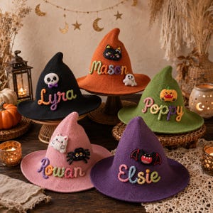 May include: Five pointed witch hats in black, orange, green, pink, and purple. Each hat features a unique embroidered name in colorful yarn and a small felt character appliqué, including a skull, cat, pumpkin, spider, and bat.