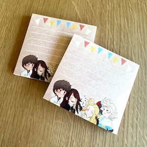 May include: Two blank lined notepads with colorful triangle designs and illustrations of cartoon characters. The characters are a group of friends with brown hair and colorful clothing.