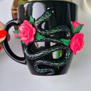 Puede incluir: Taza de cerámica negra con una serpiente verde y rosas rosas esculpidas en el lateral.