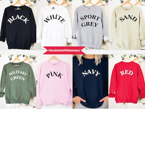 May include: Eight different coloured sweatshirts with various text printed on the front. The colours are black, white, grey, beige, green, pink, navy blue, and red. The text on the sweatshirts includes "Black", "White", "Sport Grey", "Sand", "Military Green", "Pink", "Navy", and "Red".