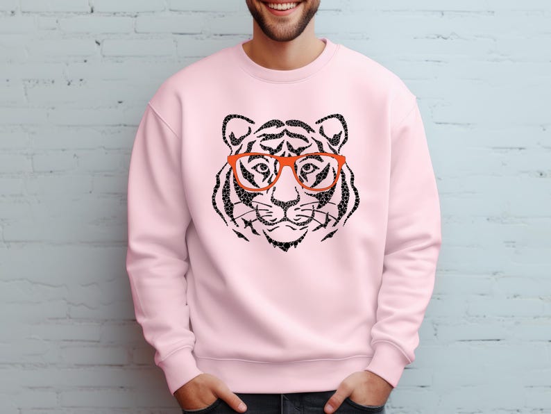 May include: A pink sweatshirt featuring a black and white tiger wearing orange glasses. The tiger is a graphic print on the front of the sweatshirt.