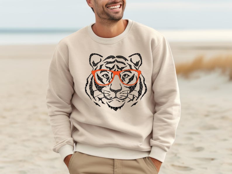 May include: A beige sweatshirt featuring a black and white graphic of a tiger wearing orange glasses.