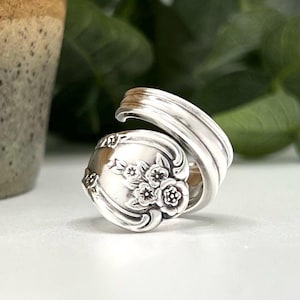 May include: A silver spoon ring with a floral design. The ring is made from a vintage spoon and is a unique piece of jewelry.