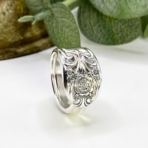 May include: A silver ring made from a vintage spoon with a floral design. The ring is wide and has a detailed rose pattern.