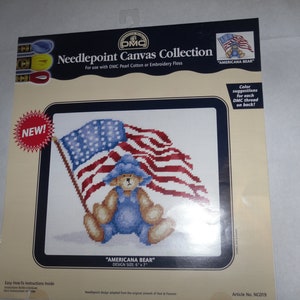 May include: Needlepoint canvas kit featuring a bear wearing a blue hat and overalls, holding an American flag. The kit is for use with DMC Pearl Cotton or Embroidery Floss. The design size is 6 inches by 7 inches. "Americana Bear" is the title of the design. "Color suggestions for each DMC thread on back!" is printed on the card. Article No. NC019.