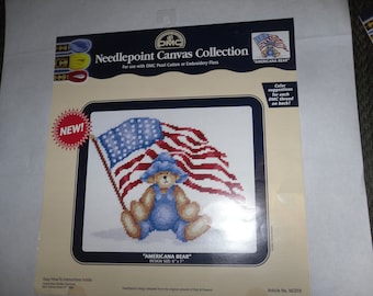 May include: Needlepoint canvas kit featuring a bear wearing a blue hat and overalls, holding an American flag. The kit is for use with DMC Pearl Cotton or Embroidery Floss. The design size is 6 inches by 7 inches. "Americana Bear" is the title of the design. "Color suggestions for each DMC thread on back!" is printed on the card. Article No. NC019.