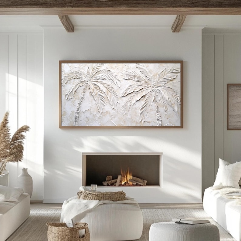 May include: A white textured wall art piece featuring two palm trees in a raised relief design. The artwork is framed in a light brown wood frame and is displayed on a white wall above a fireplace.