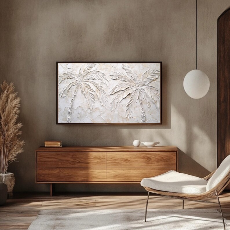 May include: A white textured wall art piece depicting two palm trees with raised relief. The art is framed in a thin black frame and hangs on a beige wall above a wooden dresser.