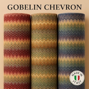 Puede incluir: Tres rollos de tela con un patrón de chevron en tonos de rojo, verde, amarillo y azul. El texto "GOBELIN CHEVRON" está en la parte superior. La tela está etiquetada como "MADE IN ITALY".