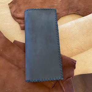 May include: A dark blue leather pouch with a stitched edge. The pouch is lying on a brown leather surface.