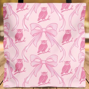 May include: Pink tote bag with a repeating pattern of pink owls perched on branches and pink bows. The bag has black handles and is made of a soft material. The background is blurred.