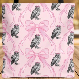 Może przedstawiać: Różowa torba z powtarzającym się wzorem szarych sów w różowych koronach z kwiatów i różowych kokardkach. Torba ma czarne uchwyty. Tło to rozmyte jesienne liście, na drewnianej powierzchni.