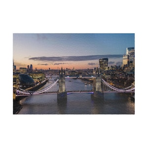 May include: An aerial view of the Tower Bridge in London at dusk. The bridge is lit with white lights, and the city skyline is visible in the background. The sky is a mix of blue, orange, and purple.