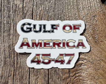 May include: A white sticker with the text "GULF OF AMERICA 45-47" in red, white, and blue lettering. The letters are outlined in silver and have a distressed, vintage look.