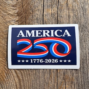 May include: A rectangular sticker with a navy blue background and white border. The word "AMERICA" is at the top in white capital letters. Below, the number "250" is stylized with red, white, and blue ribbons. The text "1776-2026" is at the bottom, with stars.