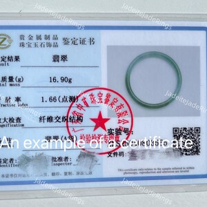 Puede incluir: Un anillo de jade jadeíta descansa sobre un certificado. El certificado, en una funda transparente, presenta texto chino, un sello rojo y un código QR. El anillo es de color verde claro.