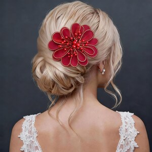 May include: A striking red flower hair clip with a beaded centre and gold trim, set against blonde hair. The hair accessory is a bold statement piece, ideal for weddings or special occasions. The flower is approximately 10 cm in diameter.