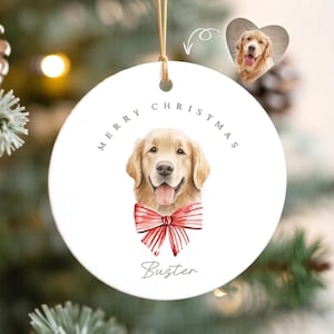 May include: White ceramic Christmas ornament with a watercolor illustration of a golden retriever wearing a red bow tie. The ornament says "Merry Christmas" and "Buster" in grey text.