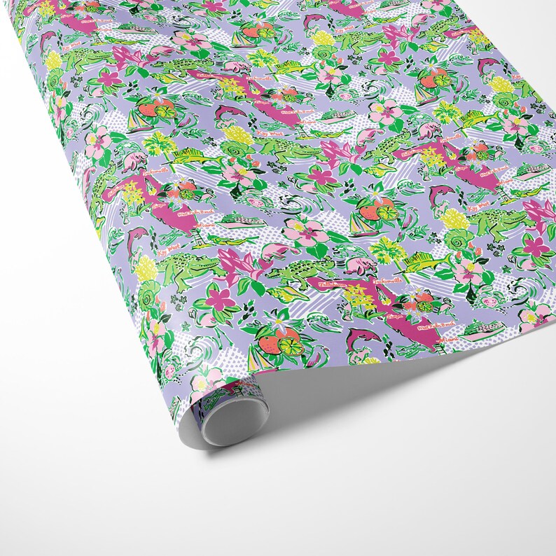 a gift wrapped in vibrant Florida-themed wrapping paper with playful illustrations of alligators, palm trees, and tropical flowers on a lavender background. A crisp white ribbon tied into a bow adds an elegant touch to the lively gift wrap.