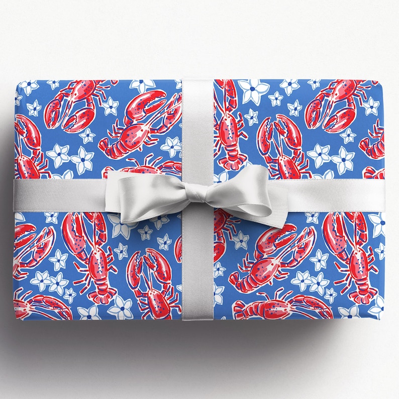 a gift wrapped in vibrant, preppy wrapping paper featuring bold red lobsters and white flowers on a blue background. The lively design is complemented by a crisp white ribbon, adding a touch of elegance to the playful gift wrap.