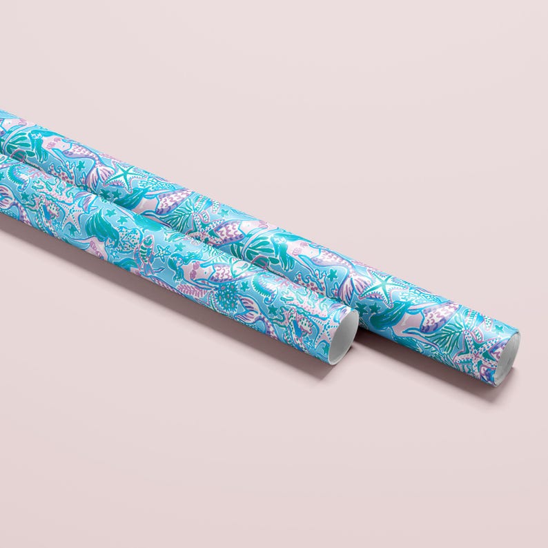 a gift wrapped in vibrant mermaid-themed wrapping paper featuring playful mermaids, sea creatures, and starfish in shades of blue, pink, and teal. A crisp white ribbon tied into a bow adds an elegant contrast to the whimsical gift wrap.