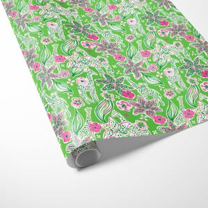 a gift wrapped in vibrant, tropical-themed wrapping paper featuring pink and white flowers and playful giraffes on a bright green background. A crisp white ribbon tied into a bow adds a classic, elegant touch to the lively and fun design.