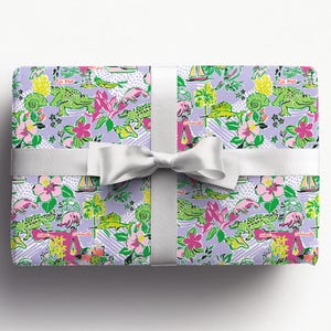 a gift wrapped in vibrant Florida-themed wrapping paper with playful illustrations of alligators, palm trees, and tropical flowers on a lavender background. A crisp white ribbon tied into a bow adds an elegant touch to the lively gift wrap.