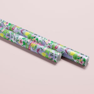 a gift wrapped in vibrant Florida-themed wrapping paper with playful illustrations of alligators, palm trees, and tropical flowers on a lavender background. A crisp white ribbon tied into a bow adds an elegant touch to the lively gift wrap.