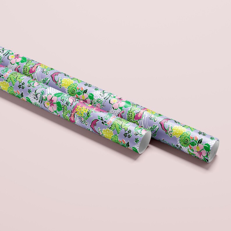 a gift wrapped in vibrant Florida-themed wrapping paper with playful illustrations of alligators, palm trees, and tropical flowers on a lavender background. A crisp white ribbon tied into a bow adds an elegant touch to the lively gift wrap.