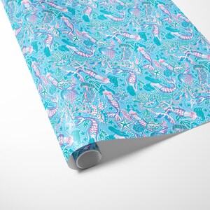 a gift wrapped in vibrant mermaid-themed wrapping paper featuring playful mermaids, sea creatures, and starfish in shades of blue, pink, and teal. A crisp white ribbon tied into a bow adds an elegant contrast to the whimsical gift wrap.