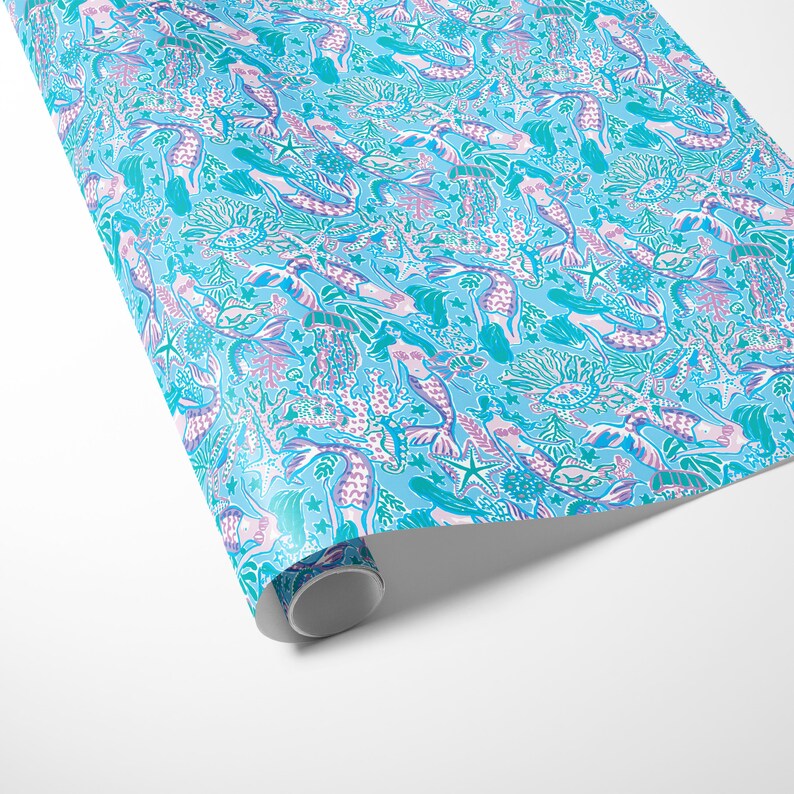 a gift wrapped in vibrant mermaid-themed wrapping paper featuring playful mermaids, sea creatures, and starfish in shades of blue, pink, and teal. A crisp white ribbon tied into a bow adds an elegant contrast to the whimsical gift wrap.