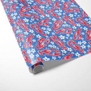 a gift wrapped in vibrant, preppy wrapping paper featuring bold red lobsters and white flowers on a blue background. The lively design is complemented by a crisp white ribbon, adding a touch of elegance to the playful gift wrap.
