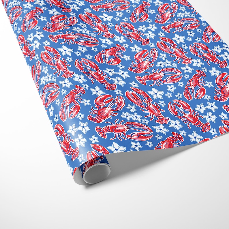 a gift wrapped in vibrant, preppy wrapping paper featuring bold red lobsters and white flowers on a blue background. The lively design is complemented by a crisp white ribbon, adding a touch of elegance to the playful gift wrap.