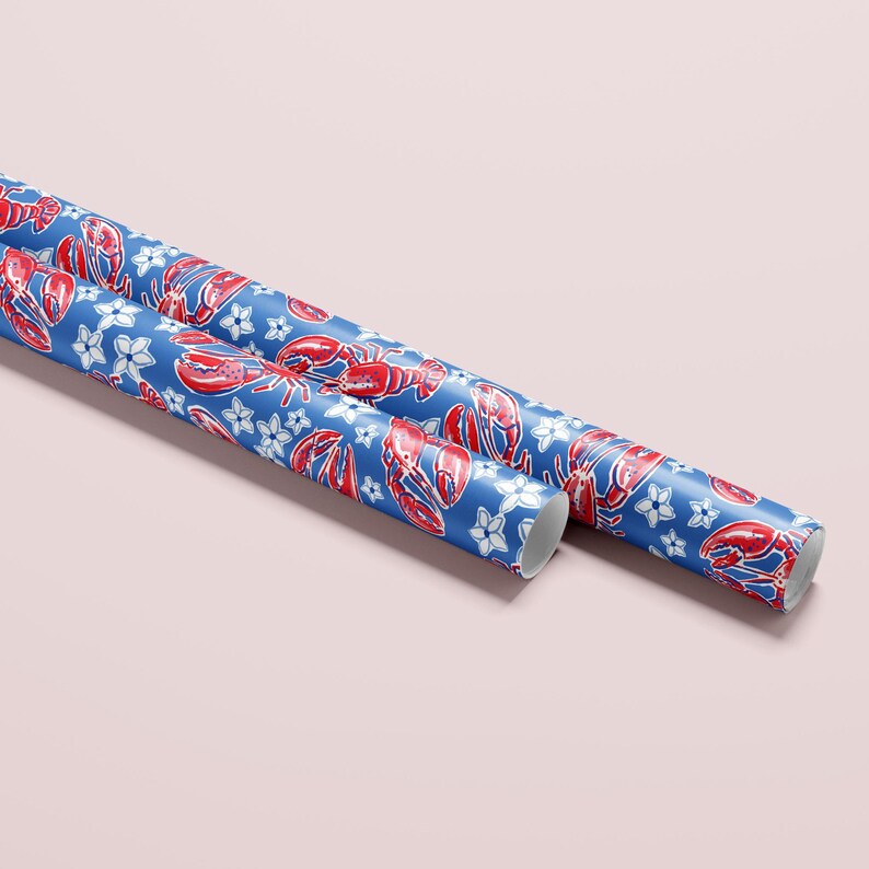 a gift wrapped in vibrant, preppy wrapping paper featuring bold red lobsters and white flowers on a blue background. The lively design is complemented by a crisp white ribbon, adding a touch of elegance to the playful gift wrap.