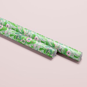 a gift wrapped in vibrant, tropical-themed wrapping paper featuring pink and white flowers and playful giraffes on a bright green background. A crisp white ribbon tied into a bow adds a classic, elegant touch to the lively and fun design.