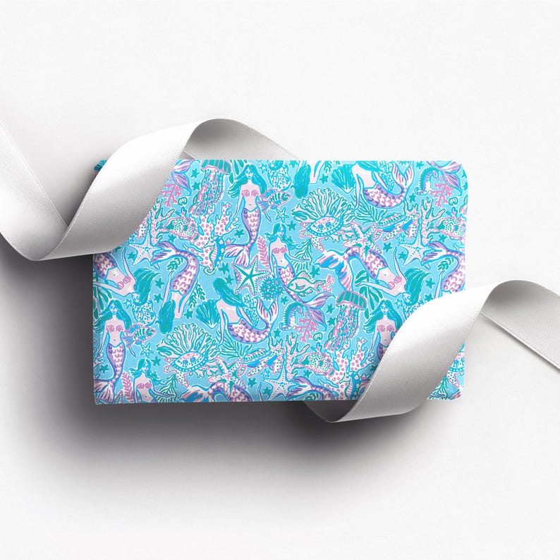 a gift wrapped in vibrant mermaid-themed wrapping paper featuring playful mermaids, sea creatures, and starfish in shades of blue, pink, and teal. A crisp white ribbon tied into a bow adds an elegant contrast to the whimsical gift wrap.
