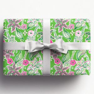 a gift wrapped in vibrant, tropical-themed wrapping paper featuring pink and white flowers and playful giraffes on a bright green background. A crisp white ribbon tied into a bow adds a classic, elegant touch to the lively and fun design.