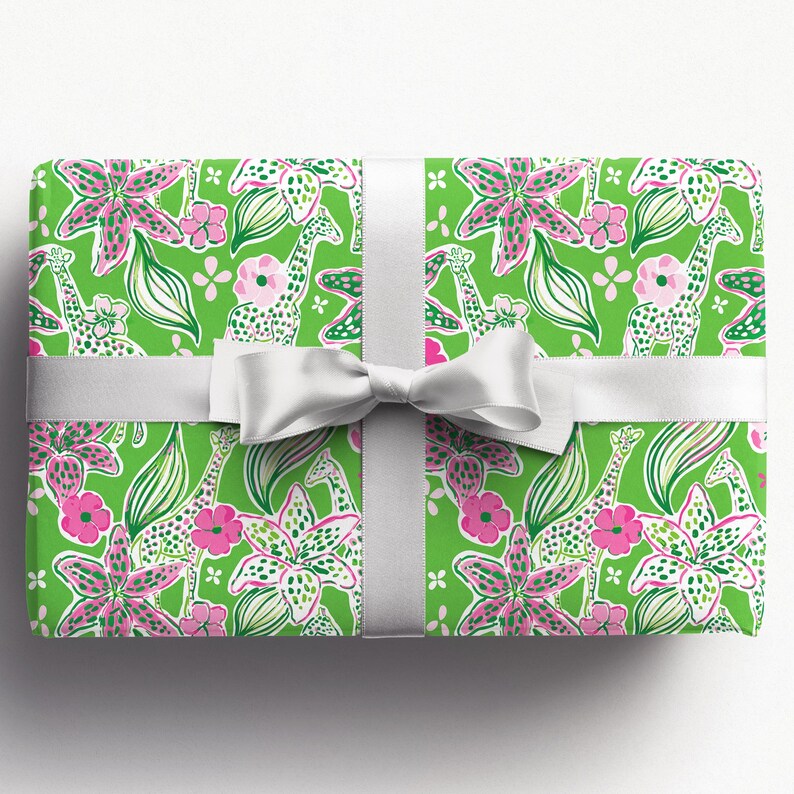 a gift wrapped in vibrant, tropical-themed wrapping paper featuring pink and white flowers and playful giraffes on a bright green background. A crisp white ribbon tied into a bow adds a classic, elegant touch to the lively and fun design.