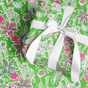a gift wrapped in vibrant, tropical-themed wrapping paper featuring pink and white flowers and playful giraffes on a bright green background. A crisp white ribbon tied into a bow adds a classic, elegant touch to the lively and fun design.