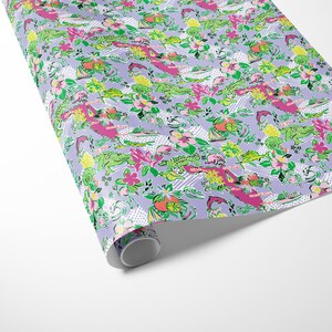 a gift wrapped in vibrant Florida-themed wrapping paper with playful illustrations of alligators, palm trees, and tropical flowers on a lavender background. A crisp white ribbon tied into a bow adds an elegant touch to the lively gift wrap.