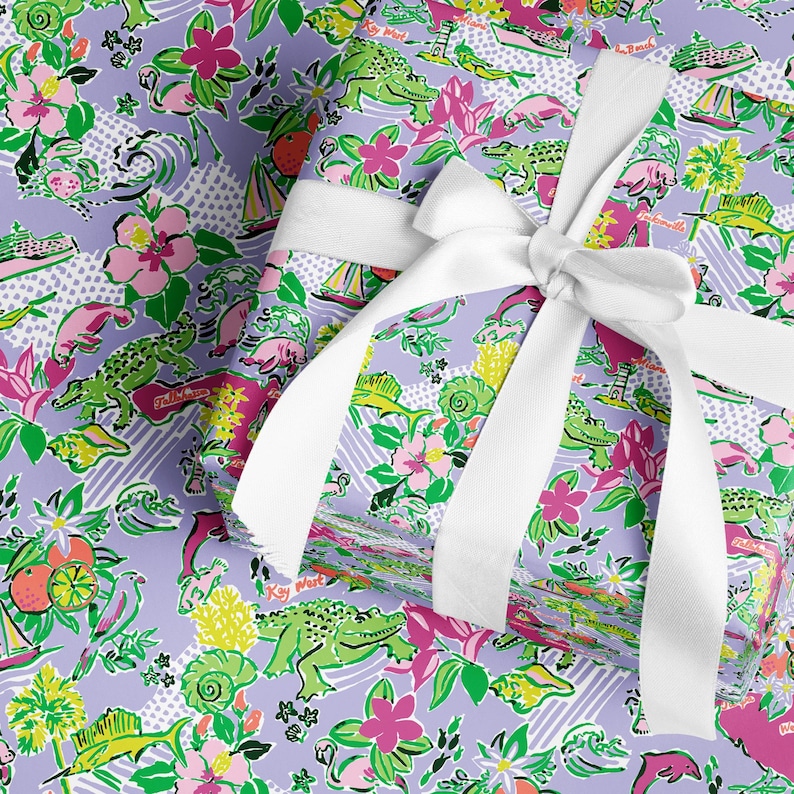 a gift wrapped in vibrant Florida-themed wrapping paper with playful illustrations of alligators, palm trees, and tropical flowers on a lavender background. A crisp white ribbon tied into a bow adds an elegant touch to the lively gift wrap.