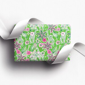 a gift wrapped in vibrant, tropical-themed wrapping paper featuring pink and white flowers and playful giraffes on a bright green background. A crisp white ribbon tied into a bow adds a classic, elegant touch to the lively and fun design.